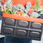 Person holding crate of fresh assorted vegetables and fruits.