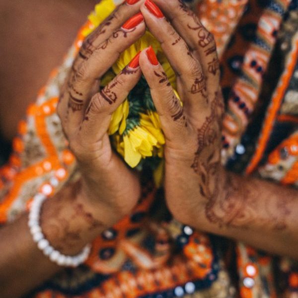 Person holding yellow flower with henna-decorated hands.