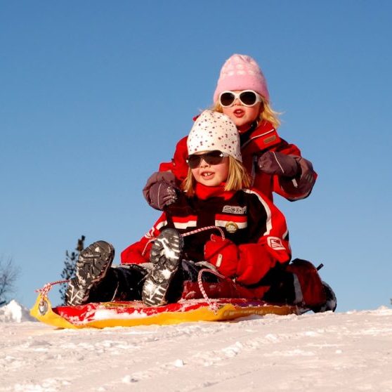 Children sledding in snow wearing sunglasses and hats.